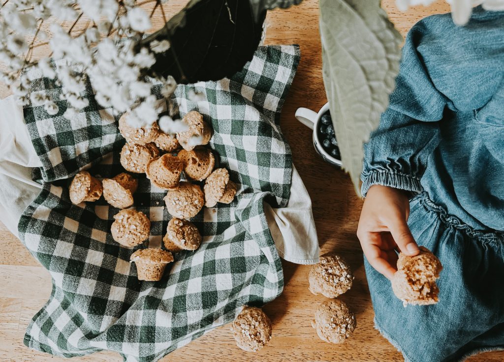 child holding an eaten muffin next to a basket of fresh milled muffins